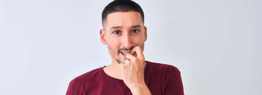 Man thinking with hand near mouth, considers veneers for crooked teeth